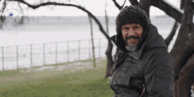 a man with a beard wears a fur hat and a black jacket