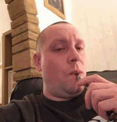 a man is smoking a cigarette while sitting on a couch in a living room .