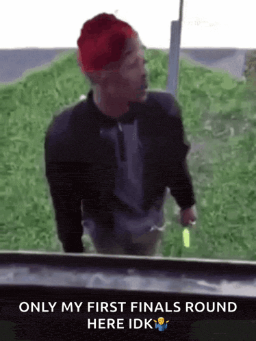 a man wearing a red hat and a black jacket is standing in front of a grassy hill .