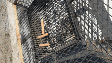 two hot dogs are sitting on a grill with a fence behind them