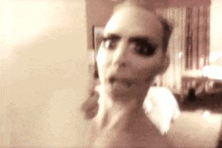a close up of a woman 's face in a room with a bed in the background .