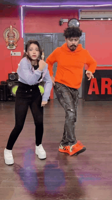 a man in an orange hoodie is dancing with a girl in a purple top