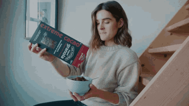 a woman is holding a box of extreme cacao granola and a bowl of cereal