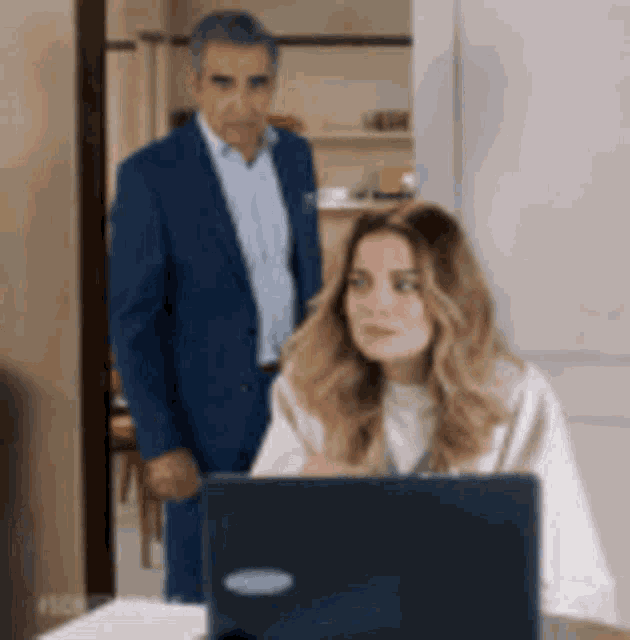 a man in a suit is standing next to a woman sitting in front of a laptop .