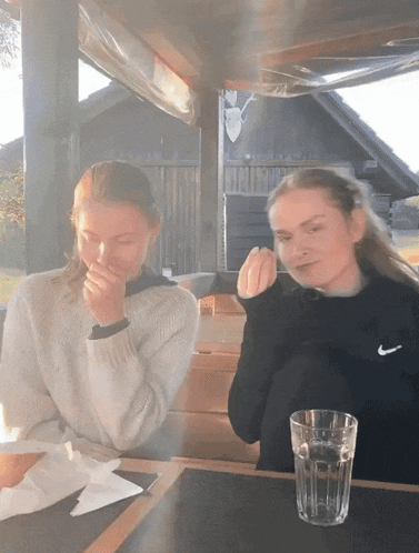 two girls sitting at a table with one wearing a nike sweater