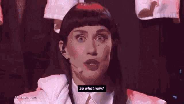 a woman with a microphone in front of her says so what now