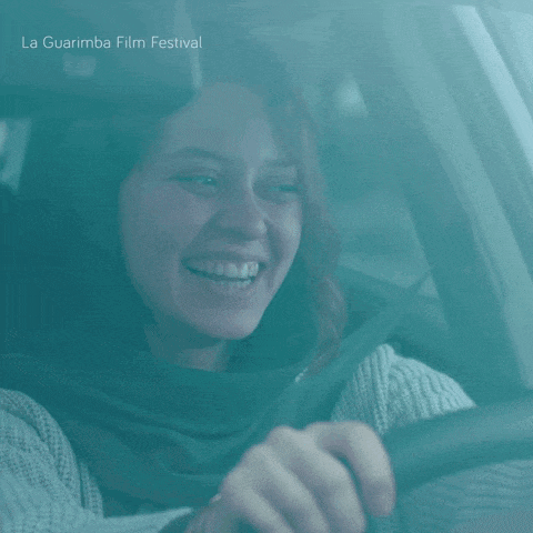 a woman is smiling while driving a car and the words la guarimba film festival are on the bottom