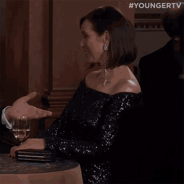 a woman in a sequined dress is talking to a man with a glass of wine
