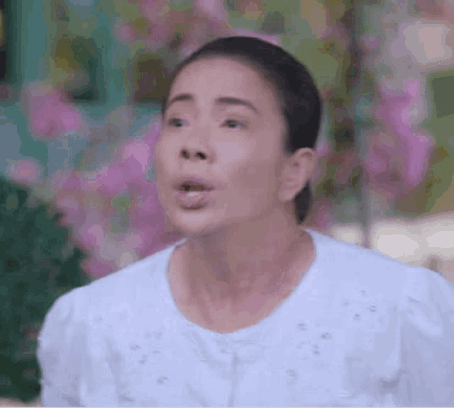 a woman in a white shirt is making a funny face while standing in front of purple flowers .
