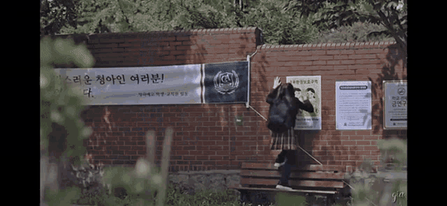 a girl sitting on a bench in front of a brick wall with a banner that says ' gs ' on it