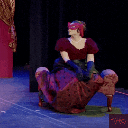 a woman wearing a mask and gloves sits on a chair on a stage