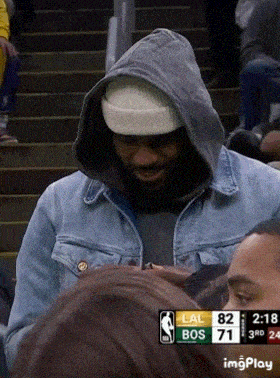 a man wearing a hooded jacket and a beanie stands in front of a scoreboard that says lal bos 71