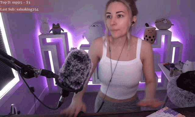 a woman in a white tank top stands in front of a microphone in a room