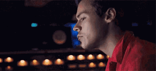 a man in a red shirt is sitting at a table in a dark room looking at something .