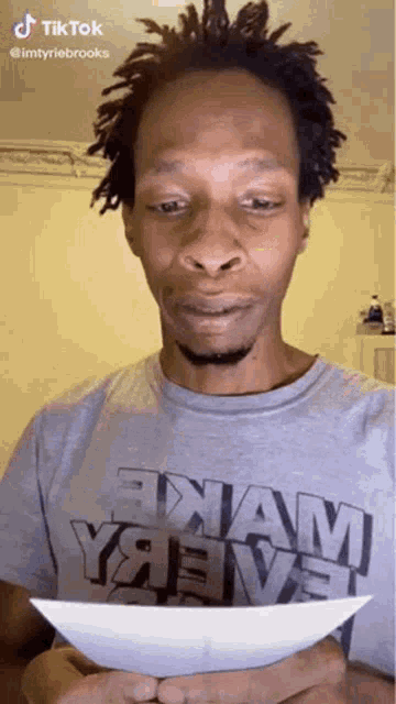 a man in a grey shirt is holding a piece of paper in his hands .