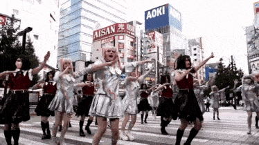 a group of people are dancing in front of a building that says aoki on it