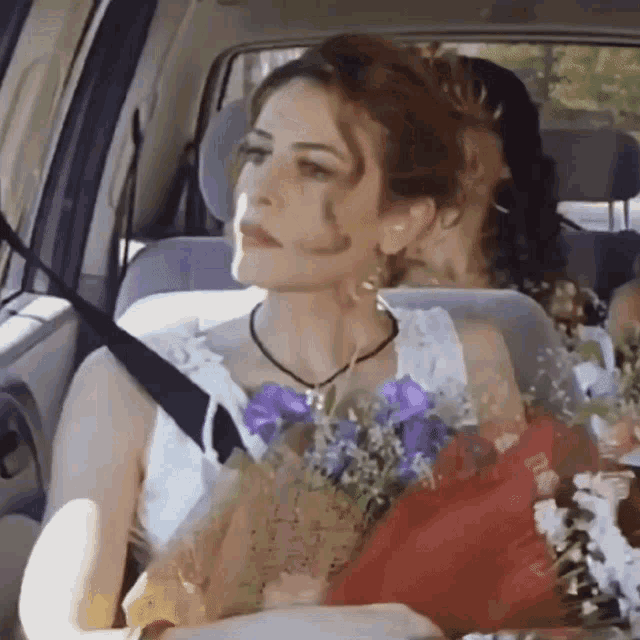 a woman in a white dress is sitting in the back seat of a car holding flowers