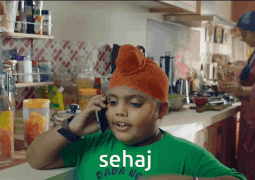 a young boy wearing an orange turban is talking on a cell phone and the word sehaj is on the shirt