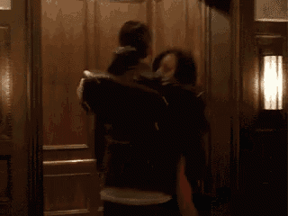 a man is carrying a woman in an elevator and kissing her on the cheek .