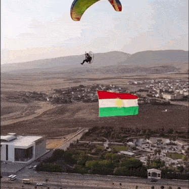a paraglider is flying over a city with a kurdish flag hanging from it