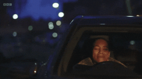 a woman is driving a car at night with the bbc logo visible