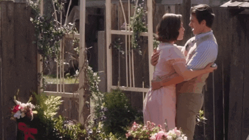 a man and woman are hugging each other in front of flowers