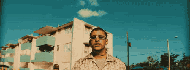 a man wearing sunglasses and a choker stands in front of a building