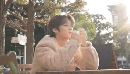 a young man in a fur coat is sitting at a table in front of a tree .