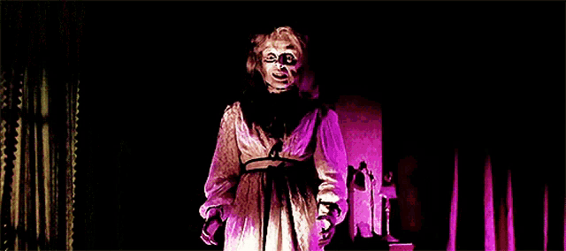 a woman in a white dress is standing in a dark room with purple curtains