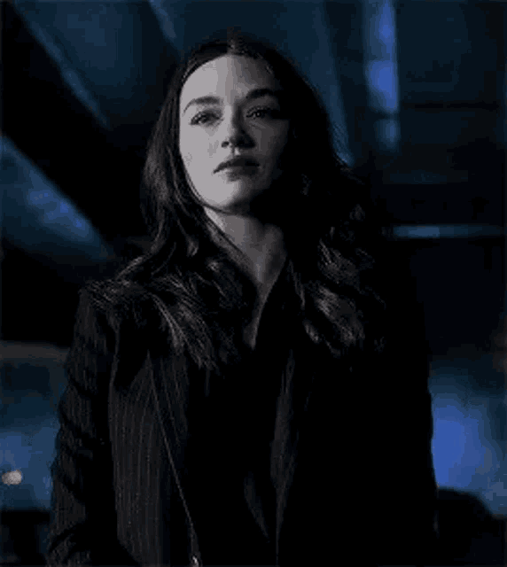 a woman in a black suit is standing in a dark room looking at the camera .