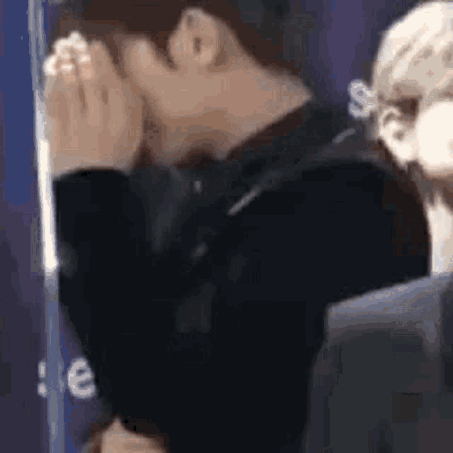 a man is covering his face with his hands while standing next to a woman in a suit .