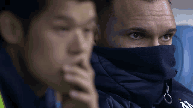 a man wearing a blue jacket with the letter a on it sits next to another man