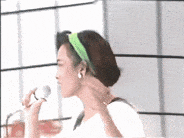 a woman wearing a green headband and earrings is singing into a microphone
