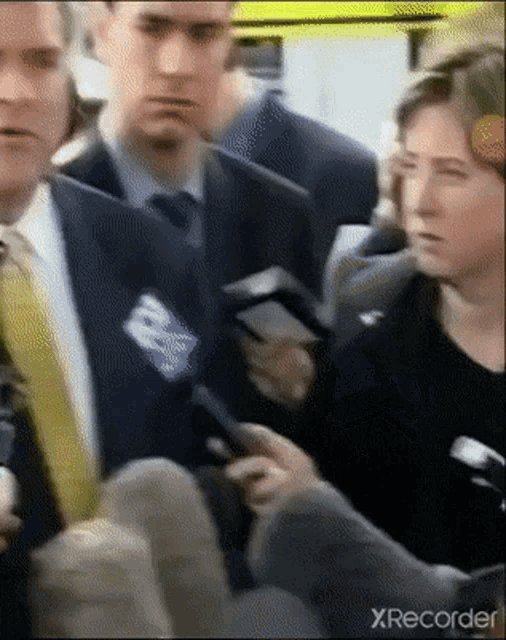 a man in a suit and tie is holding a microphone and a woman is holding a cell phone .