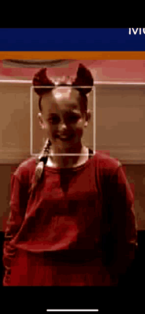 a girl in a red shirt with devil horns on her head is smiling