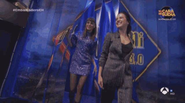 two women are dancing in front of a sign that says " el gue "