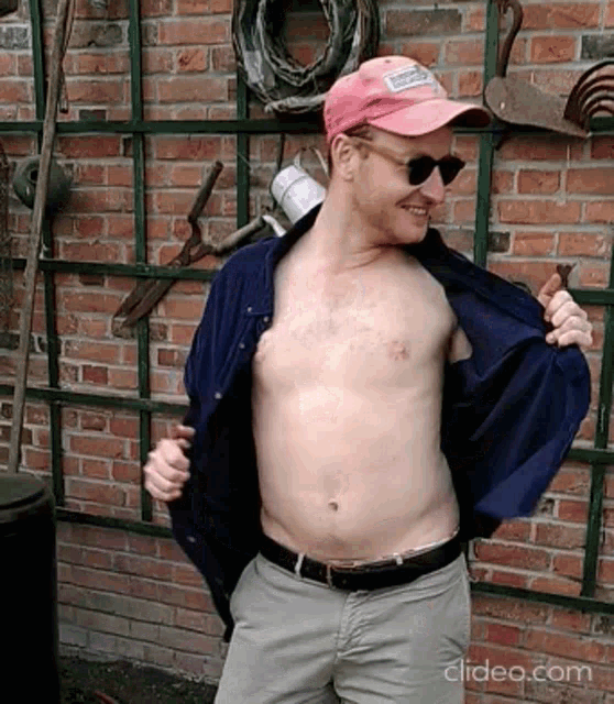 a shirtless man is standing in front of a brick wall with clipeo.com written on the bottom