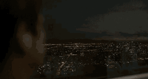 a person looking out a window at night with a city in the background
