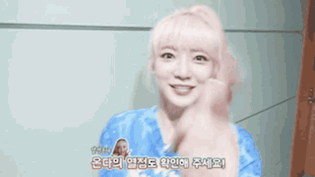 a woman with pink hair and a blue shirt giving a thumbs up