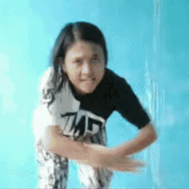 a girl wearing a shirt that says tmf stands in front of a blue wall