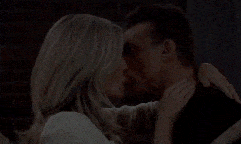 a man and woman kiss in front of a brick wall