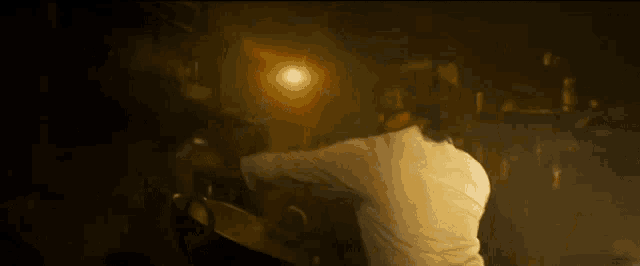 a man in a white shirt is standing in a dark room holding a pan .