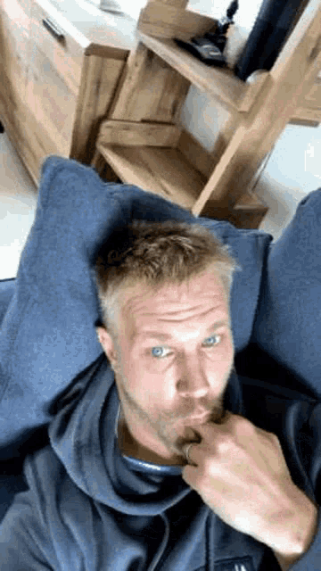 a man with blue eyes is sitting on a blue couch with his hand on his chin .
