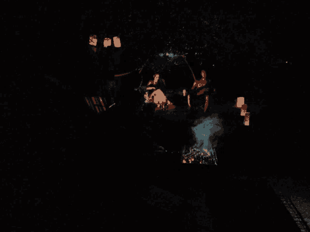 a group of people sitting around a fire with lanterns hanging from the trees