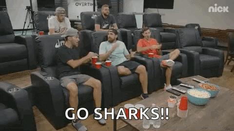 a group of men are sitting in a theater watching a game and talking .