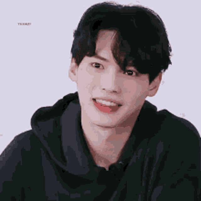 a young man wearing a black hoodie is smiling with his tongue out .
