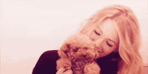 a woman is holding a small brown poodle in her arms and kissing it .