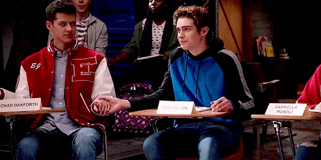 two boys holding hands in a classroom with one wearing a jacket that says ep