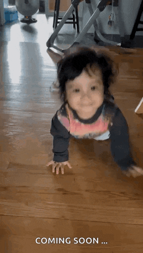 a baby is crawling on a wooden floor with the words coming soon written on the bottom .