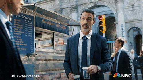 a man in a suit and tie standing in front of a food truck that says breakfast hot coffee